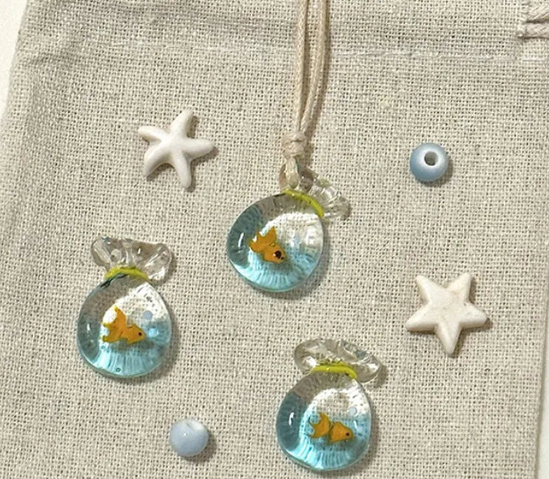 Women's necklace with small coloured glaze fish lucky bag pendant on a braided cotton and linen chain.