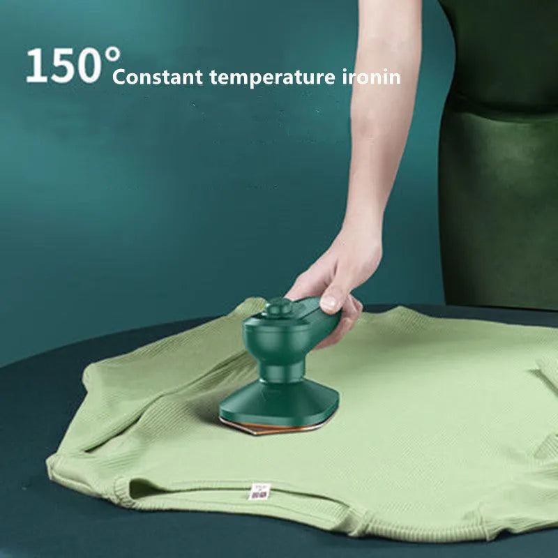 Dark green portable handheld steam iron with ceramic panel, shown next to clothing on a hanger.
