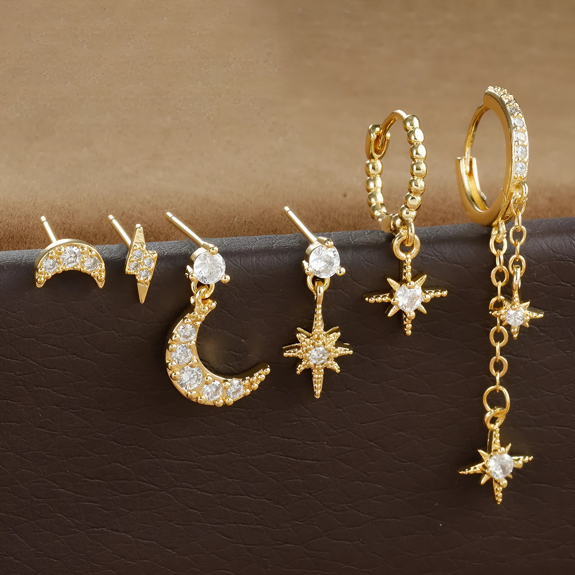 Set of six gold chain tassel drop earrings with crystal studs on a white background.