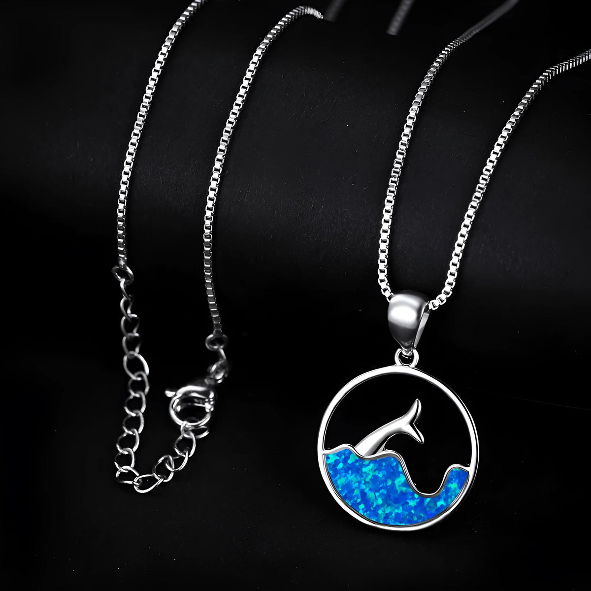 Close-up of a women's geometric fishtail necklace with a round blue opal pendant on a white gold-coloured chain.