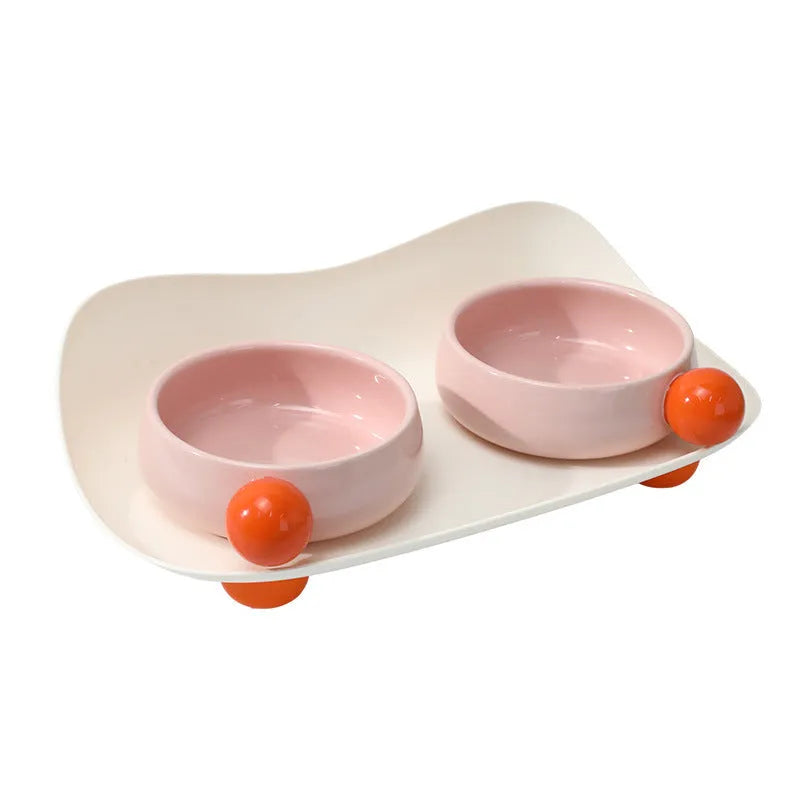 Two ceramic pet bowls on raised non-slip bases, in pink and yellow colours.