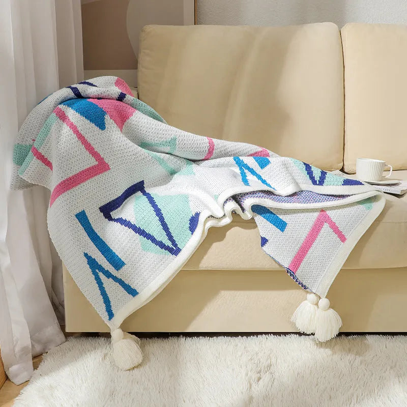 Acrylic sofa blanket with tassel fringe in neutral beige tone on grey sofa
