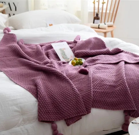 Nordic style beige acrylic throw blanket with fringed knit ball edges on a grey sofa
