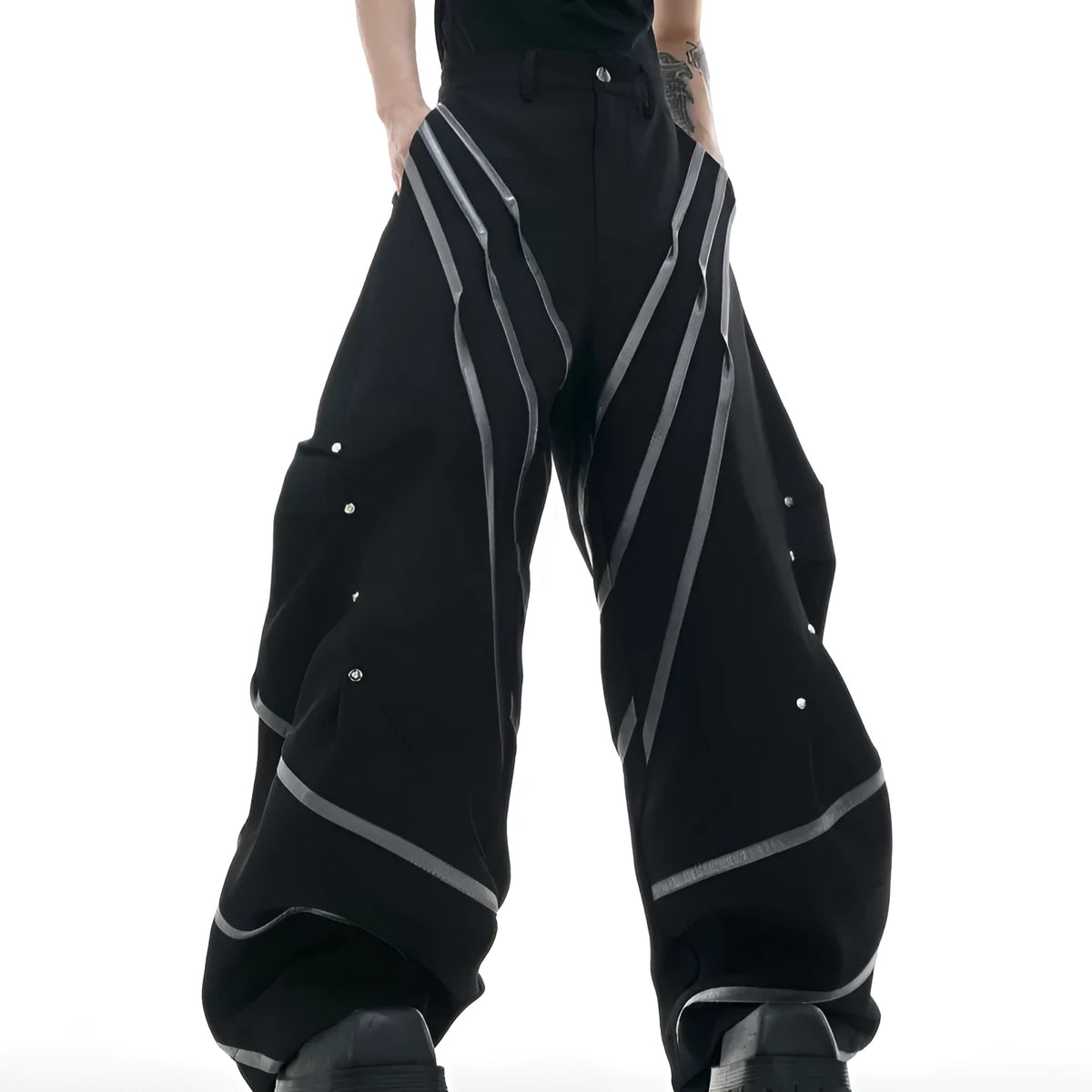Men's black trousers with structured three-dimensional cut and metal rivet pleats on the legs.