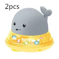 Whale-shaped electric bath toy spraying water with coloured LED lights, shown with base unit on blue background