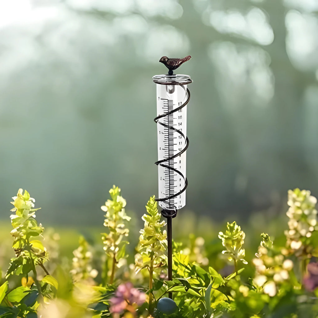 Cast iron hummingbird garden rain gauge with glass tube showing water measurement scale.