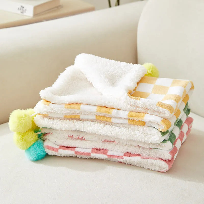 Green plaid plush fleece pet blanket with fur ball trim, laid flat as a dog bed or cat mat.