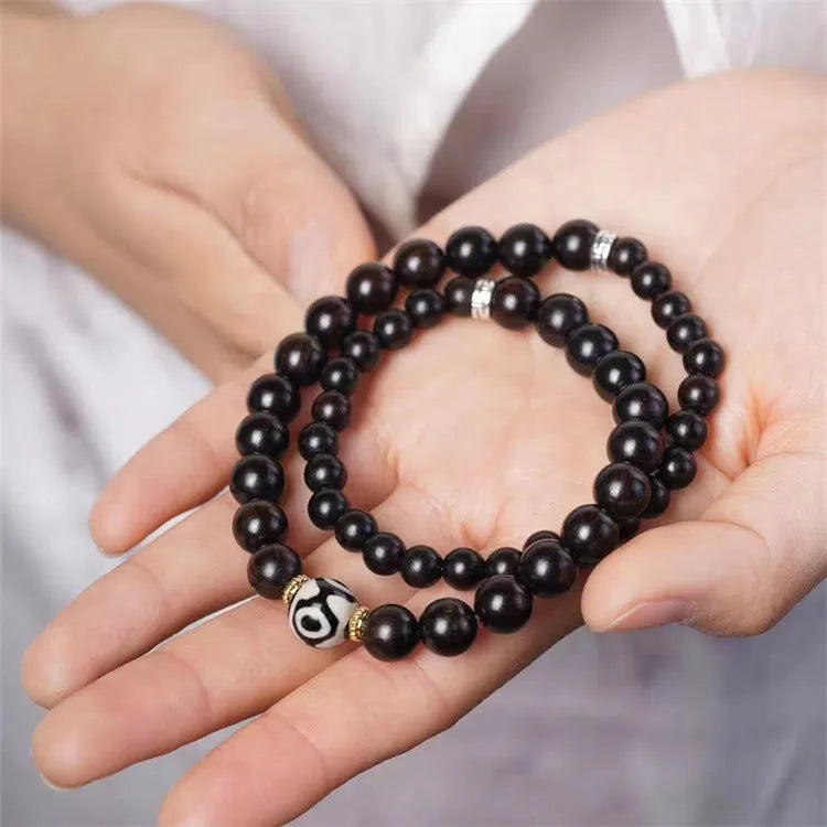 Dark ebony wood bracelet with 8mm beads in a two-circle Tibetan style on a wrist.