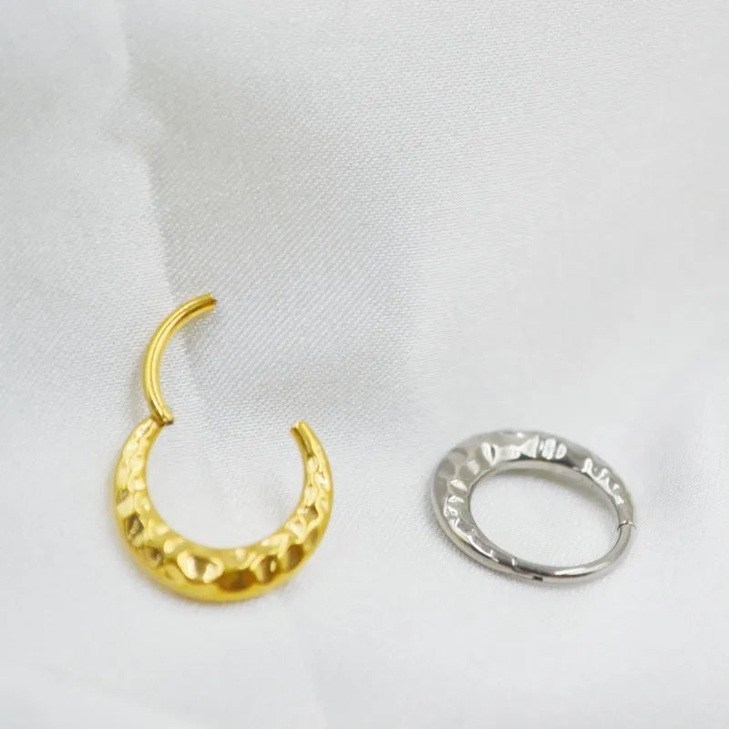 Close-up of a concave-convex carved titanium nose ring in gold and silver finishes.