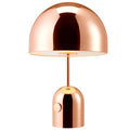 Mushroom-shaped metal table lamp in a rose gold finish on a wooden surface.