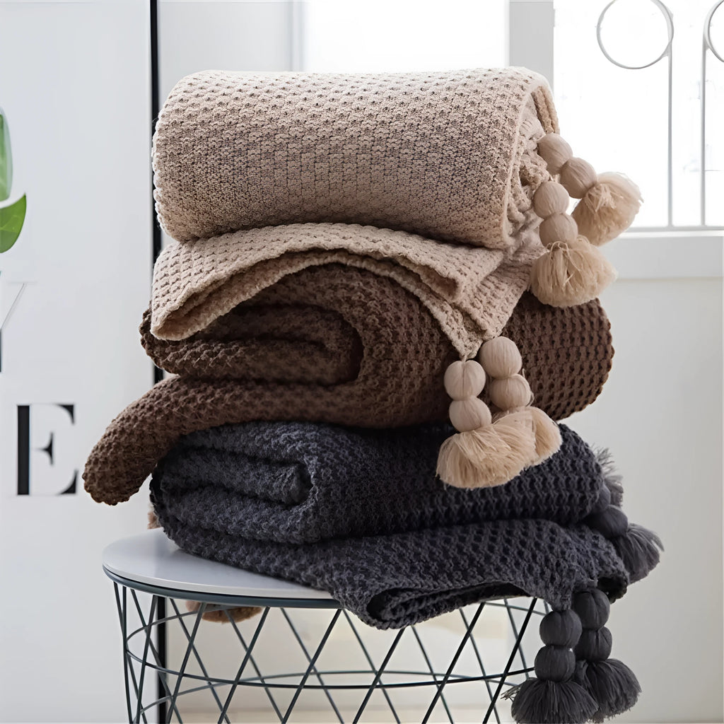 Nordic style beige acrylic throw blanket with fringed knit ball edges on a grey sofa
