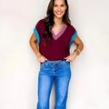 Burgundy and black loose V-neck sweater with cuffed short sleeves on a neutral background