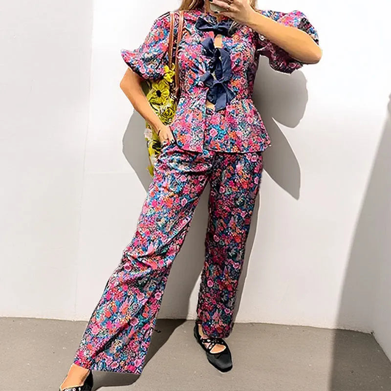 Women's floral print trouser suit set featuring a tie-neck blouse with puff sleeves and matching trousers.