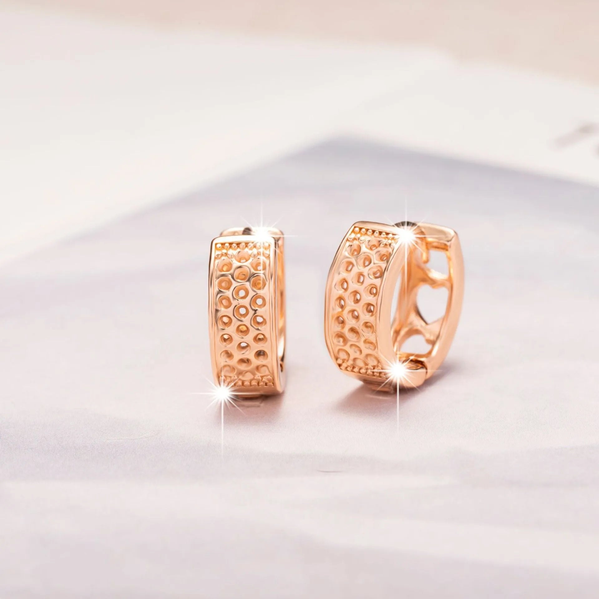 Rose gold coloured circular earrings with a hollowed-out three-heart design.