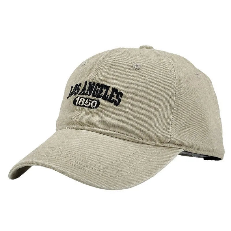 Retro style peaked cap with embroidered distressed letters on the front, shown in beige colour.