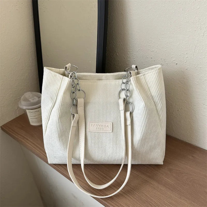 Corduroy one-shoulder tote handbag in black, showing three-dimensional pockets and a large main compartment.