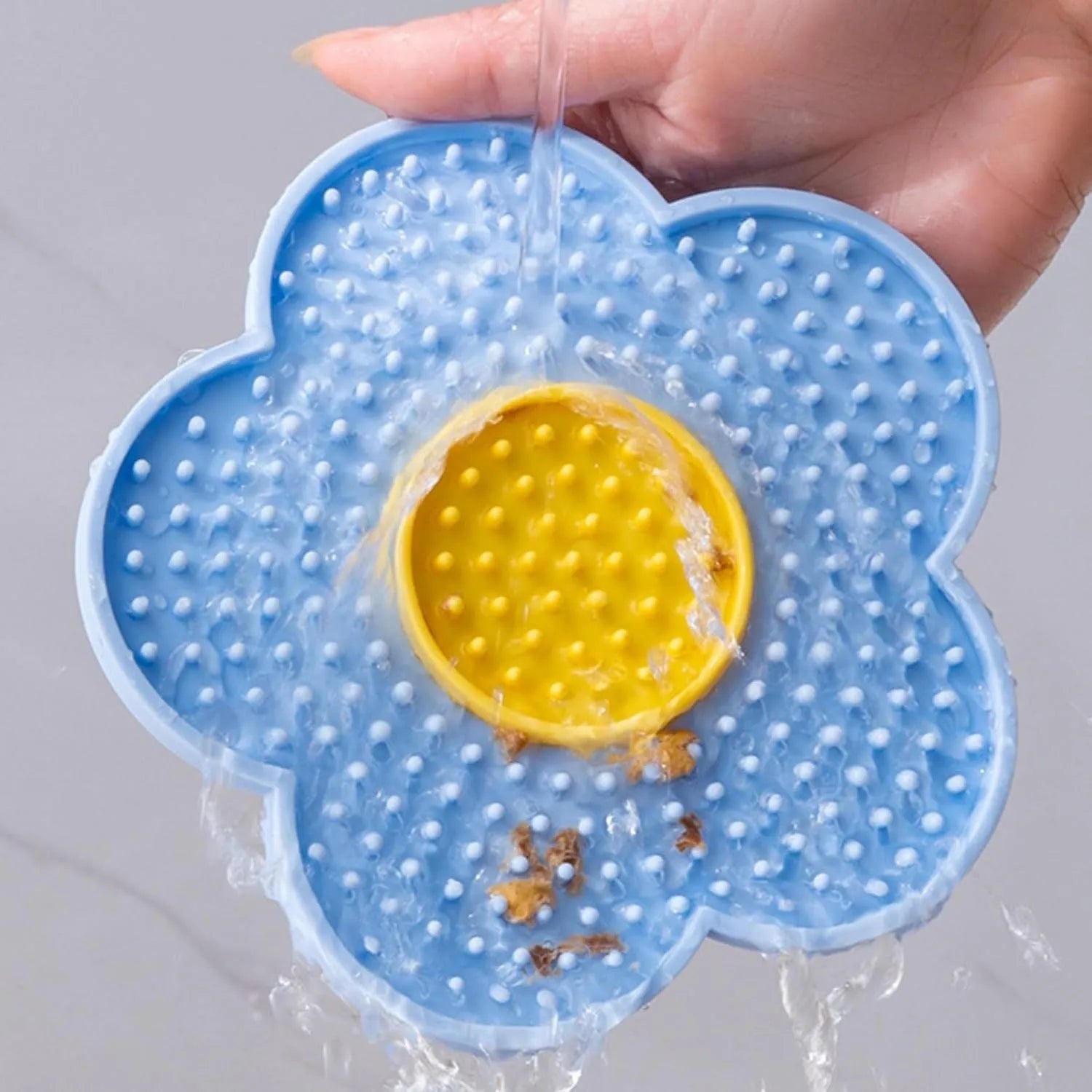 Flower-shaped blue silicone pet lick mat with suction cups on a tiled floor.