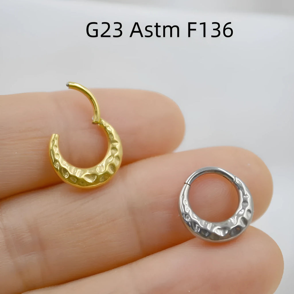 Close-up of a concave-convex carved titanium nose ring in gold and silver finishes.