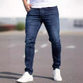Man wearing dark blue slim-fit skinny jeans with a zipper fly, showcasing the mid-waist and street fashion style.