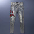 Men's blue slim fit jeans with distressed holes and embroidered patches on faded denim.