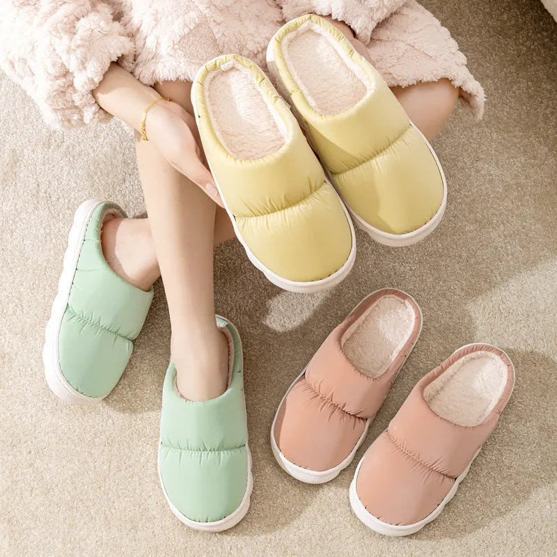 Pair of grey artificial leather slippers with a thick rubber sole and plush lining, shown on a wooden floor.