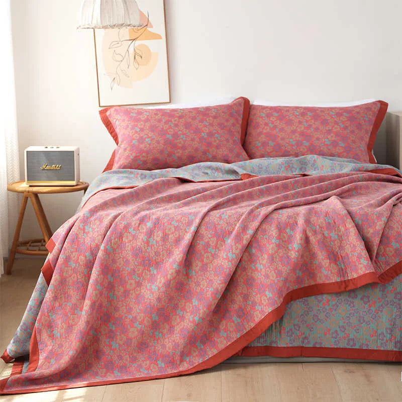 Cotton gauze floral blanket and two pillowcases set laid on a bed, showing plants and flowers pattern.