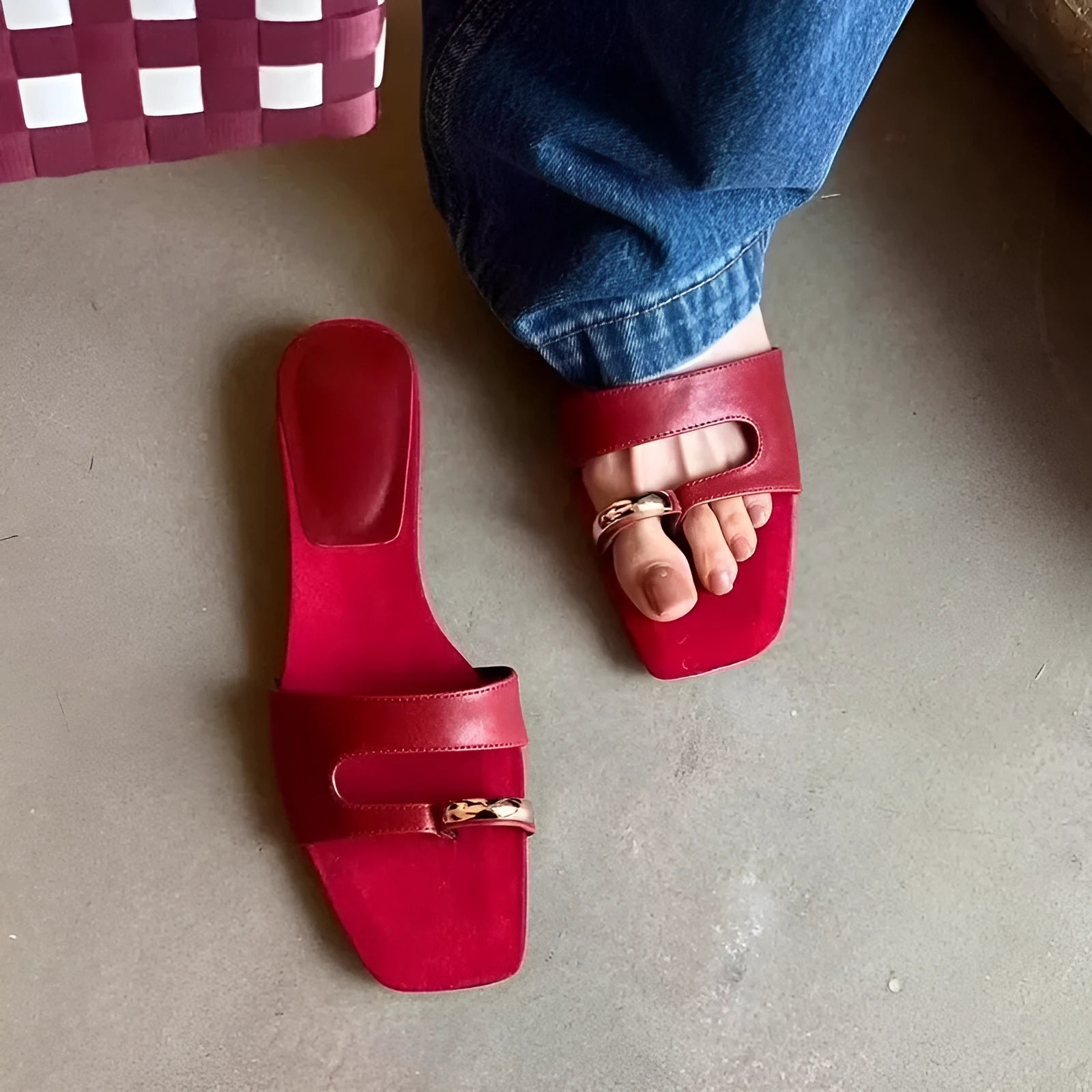 A pair of black square-toe slippers with a leather upper and light rubber sole on a wooden floor.