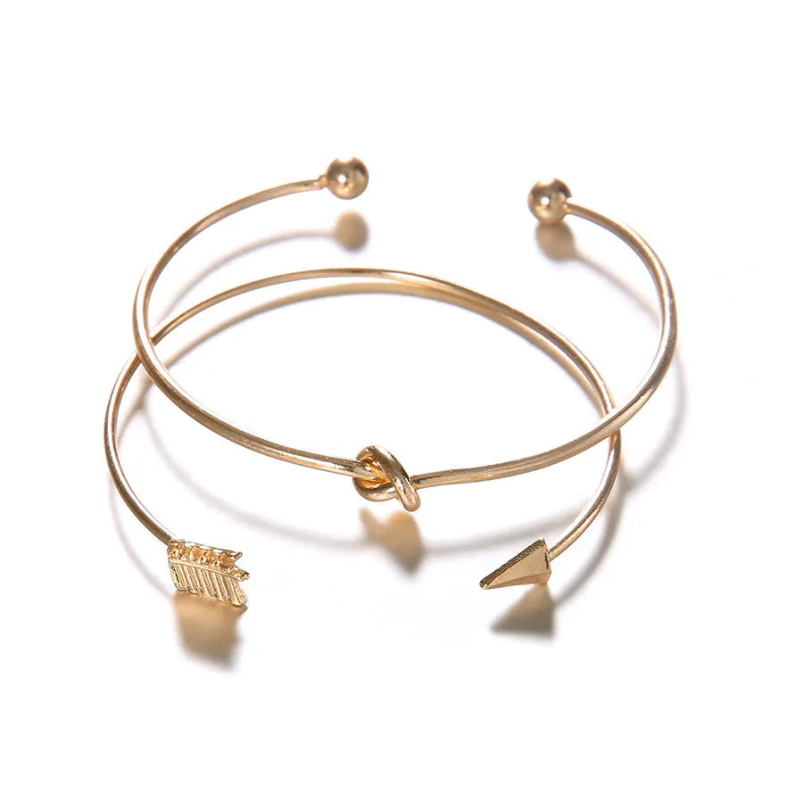 Gold electroplated alloy women's vintage cuff bracelet with knotted arrow design on a white background.