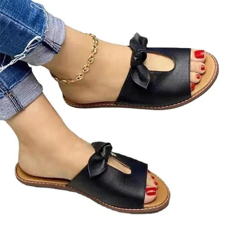 Ladies black fish mouth open-toe sandals with a gold bow detail on the strap.