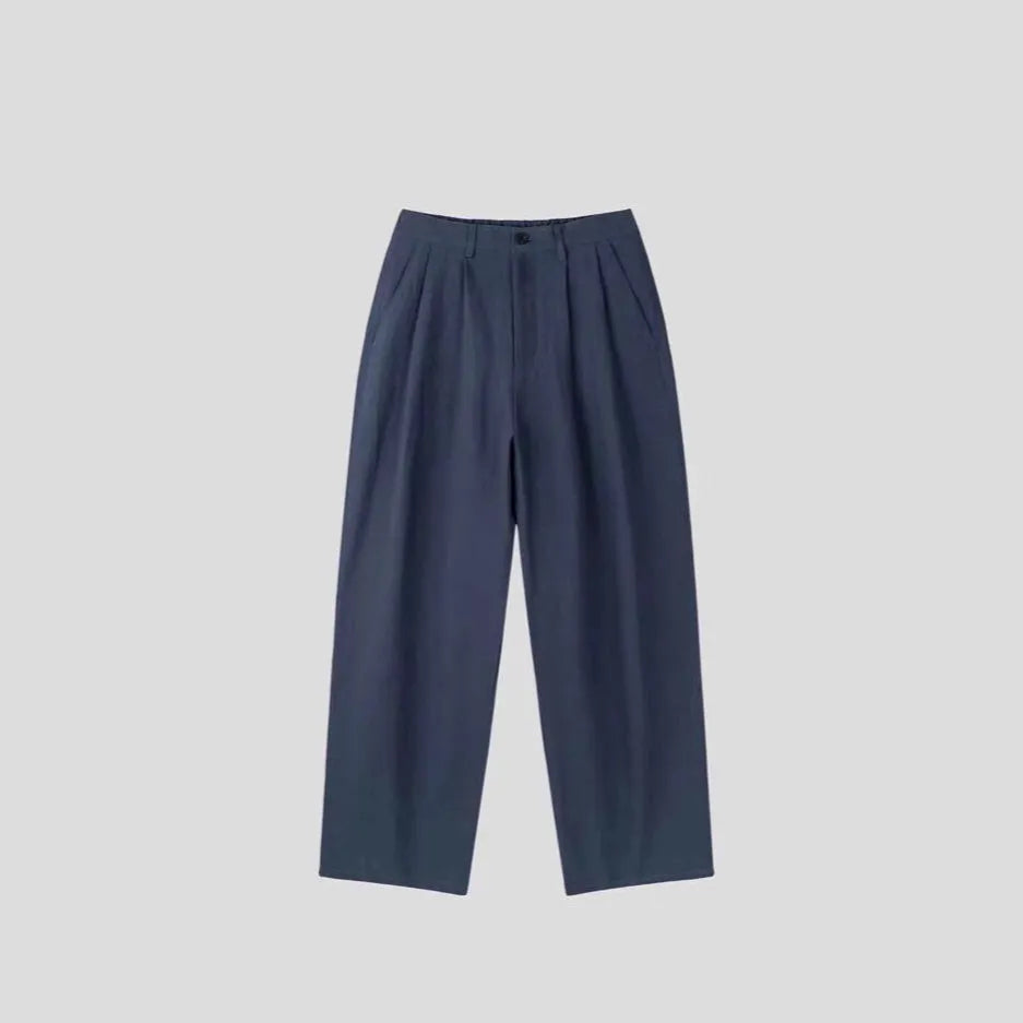 Men's apricot coloured loose-fit cotton linen trousers with a pencil leg on a plain background