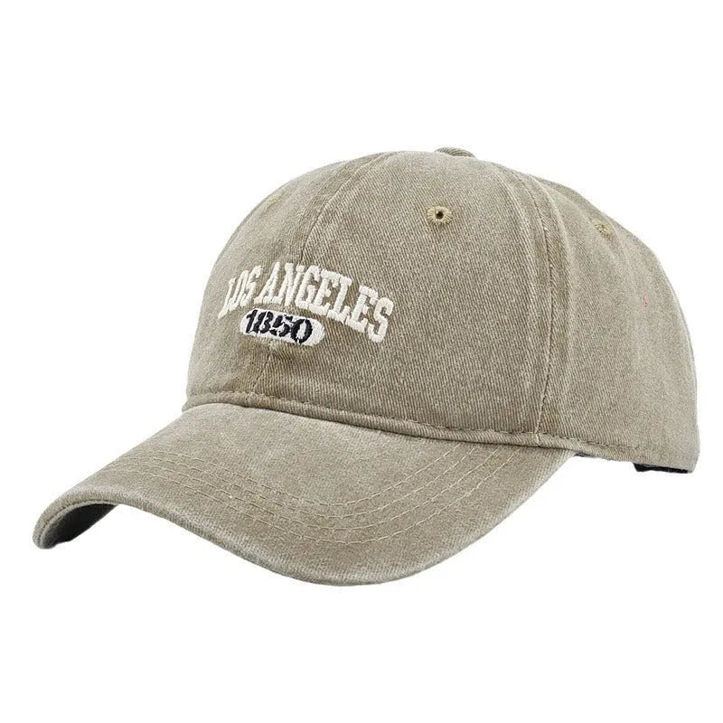 Retro style peaked cap with embroidered distressed letters on the front, shown in beige colour.