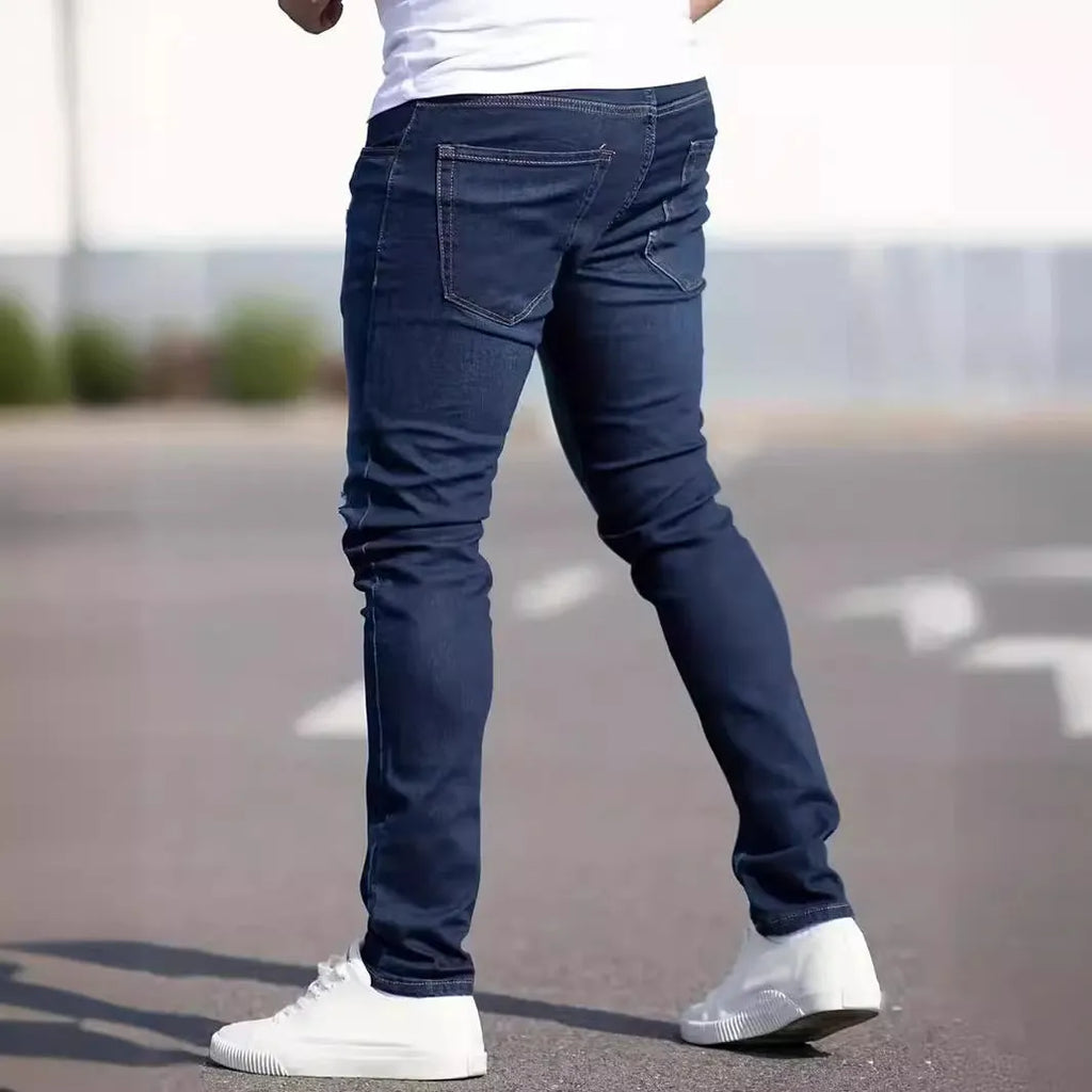 Man wearing dark blue slim-fit skinny jeans with a zipper fly, showcasing the mid-waist and street fashion style.