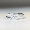 Women's geometric cross moissanite ring with twisted silver band and 1 carat stone.