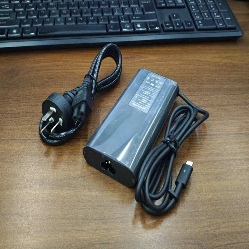 Black oval 65W USB-C laptop power adapter with UK plug, measuring 106mm long.