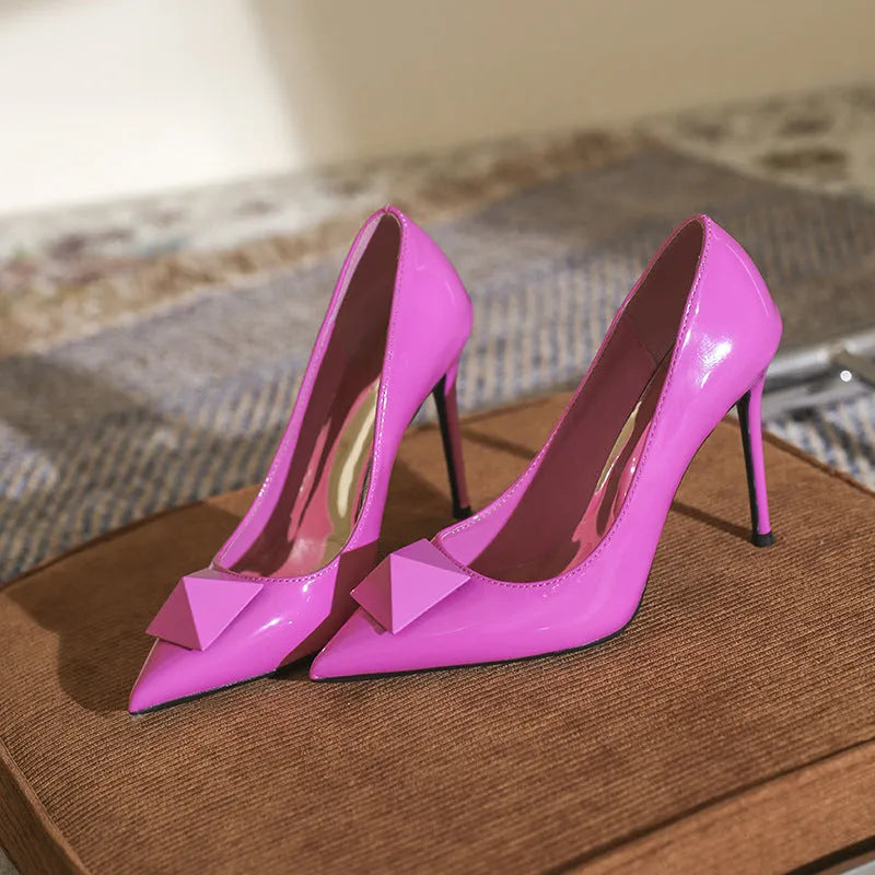 Pink patent leather women's stiletto high heels with pointed toe and metal rivet buckle detail.
