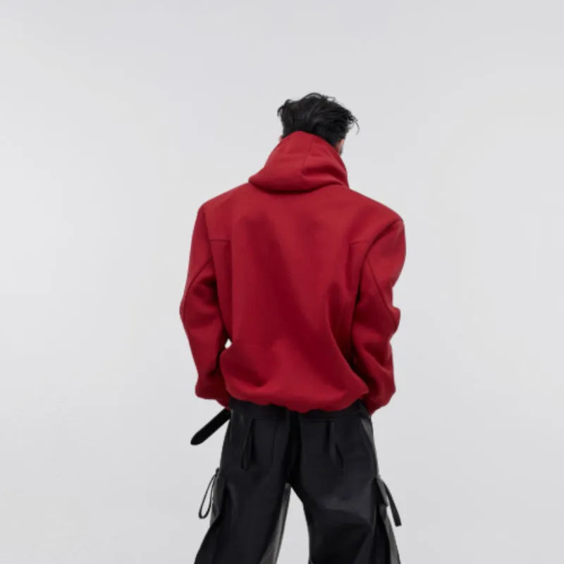A man wearing a loose red hooded sweatshirt with heavy shoulder pads and raised metal graphic printing.