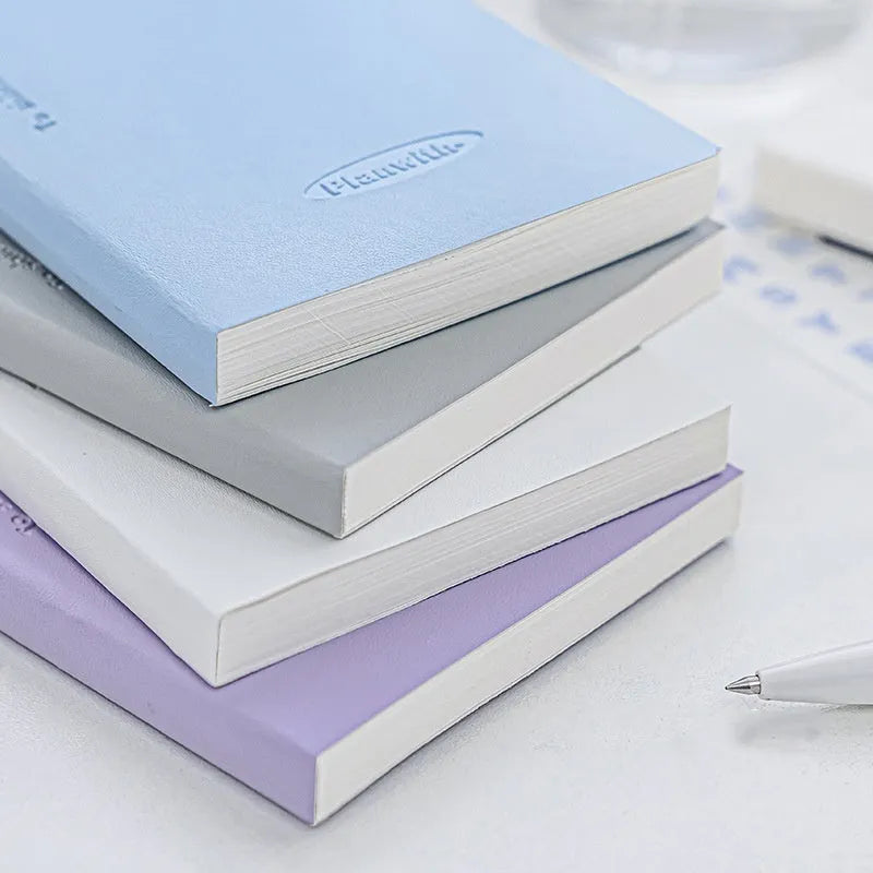A5 embossed meter notebook open on a desk, showing white 100gsm paper and a choice of five cover colours.