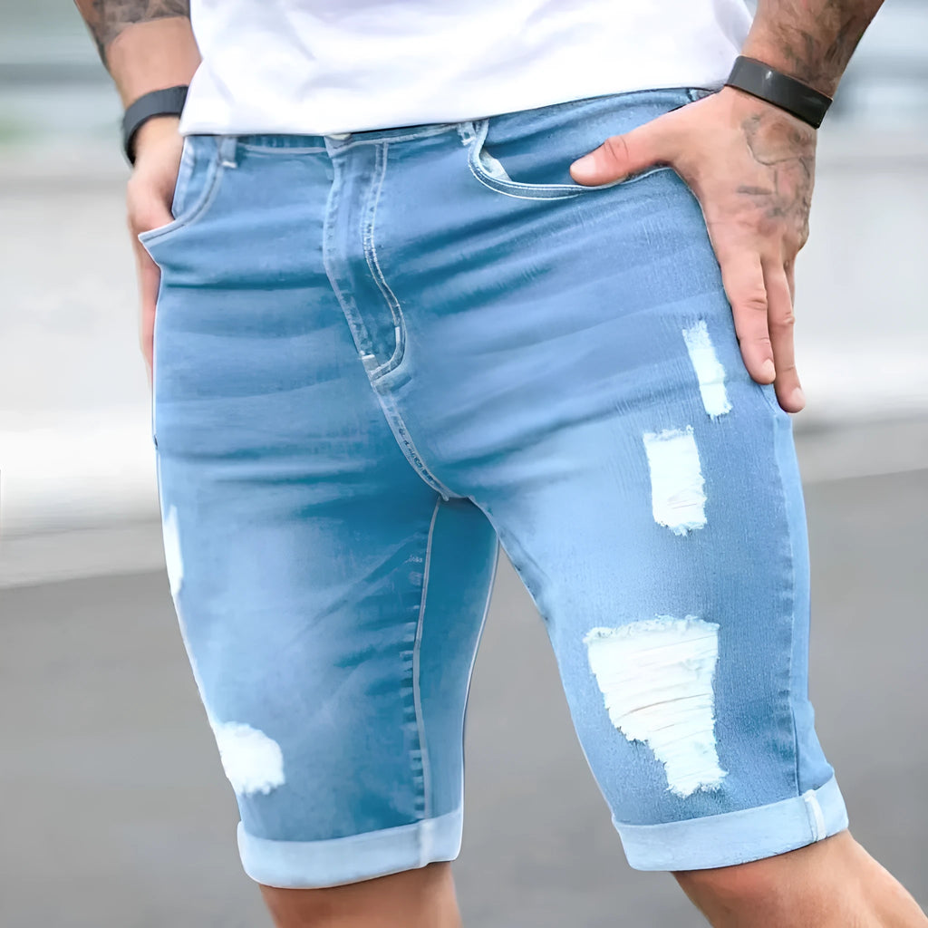 Sky blue men's denim shorts with multi-hole distressing on the legs, showing a low-rise waist and zipper fly.