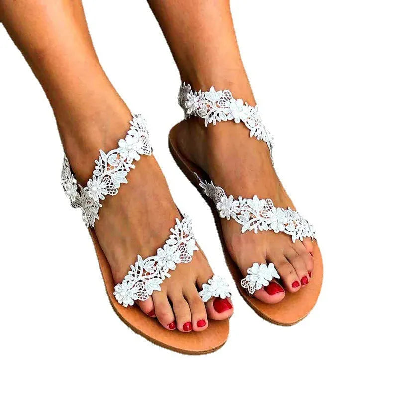 White women's flat sandals with rhinestone flower decoration on patent leather upper, showing round toe and slip-on design