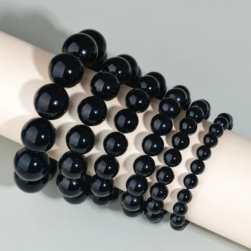 Hand-woven round obsidian bracelet in black stone, shown on a wrist.