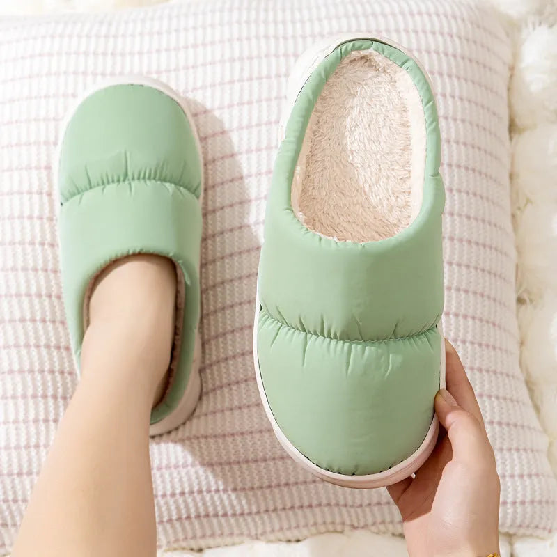 Pair of grey artificial leather slippers with a thick rubber sole and plush lining, shown on a wooden floor.