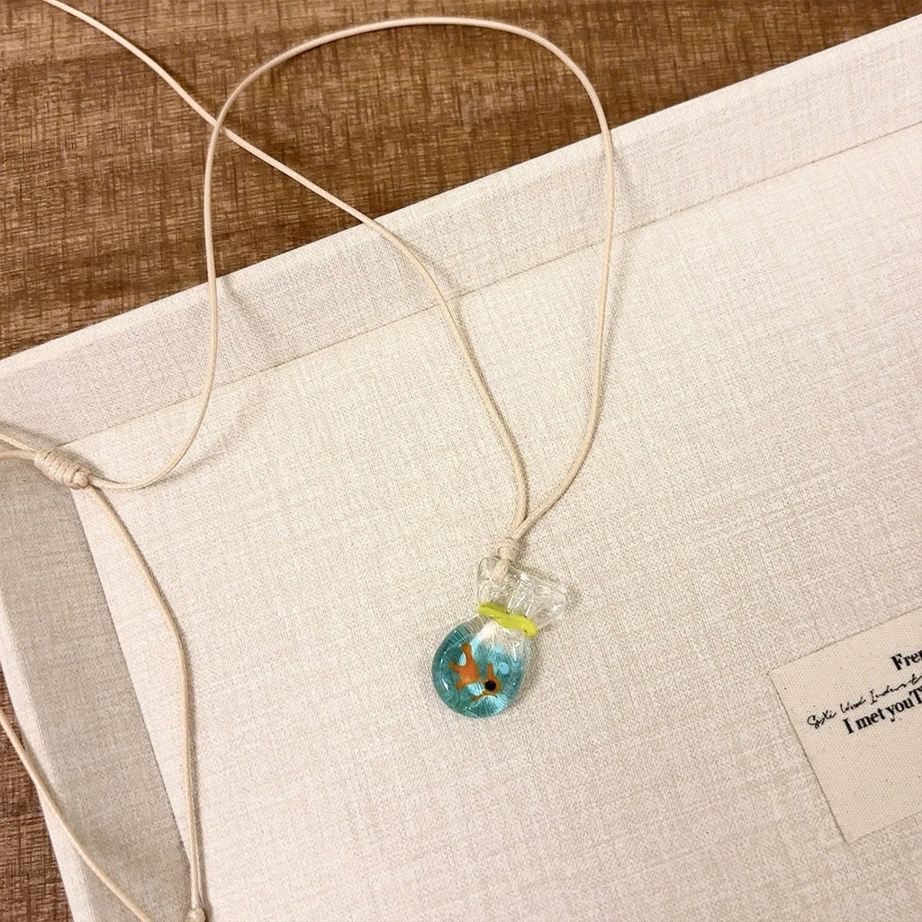 Women's necklace with small coloured glaze fish lucky bag pendant on a braided cotton and linen chain.