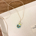 Women's necklace with small coloured glaze fish lucky bag pendant on a braided cotton and linen chain.