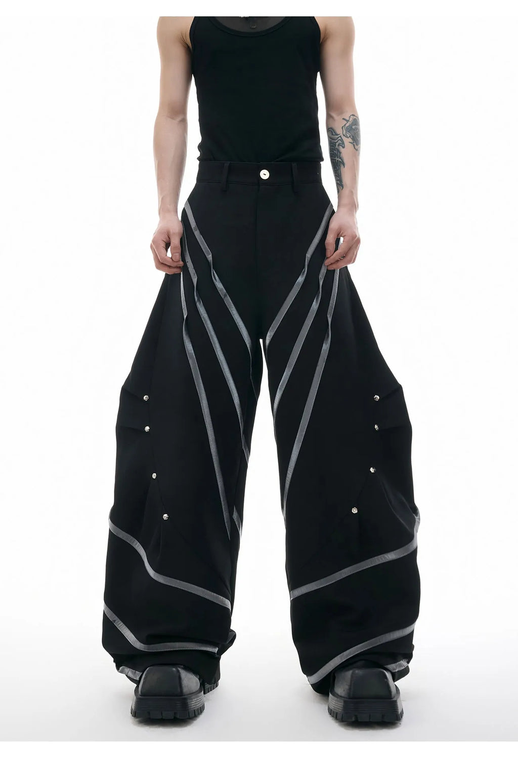 Men's black trousers with structured three-dimensional cut and metal rivet pleats on the legs.