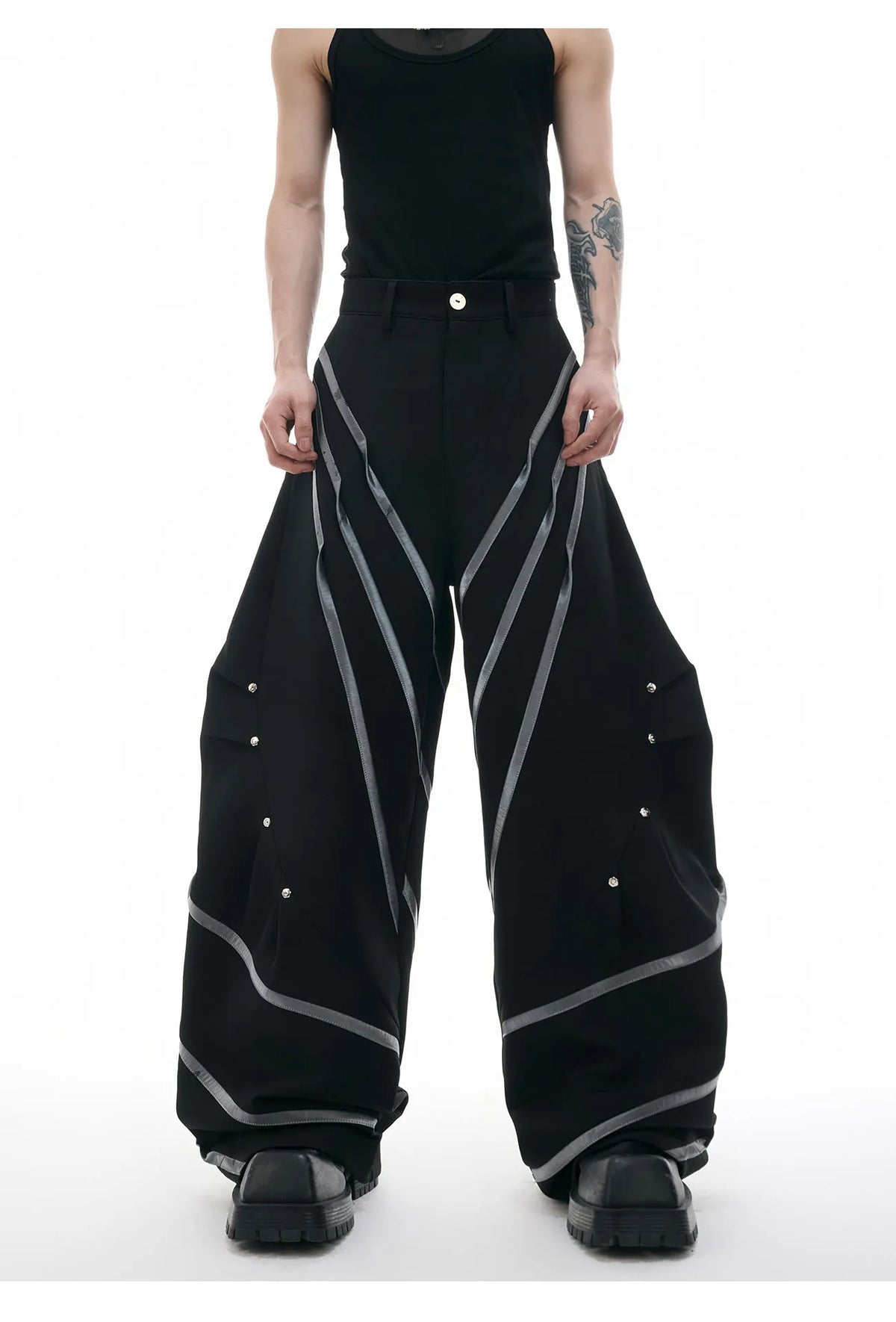 Men's black trousers with structured three-dimensional cut and metal rivet pleats on the legs.