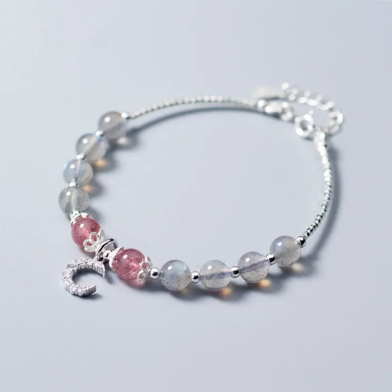 Handmade adjustable moonstone bracelet with a silver crescent moon charm and clear crystal accent on a grey background.