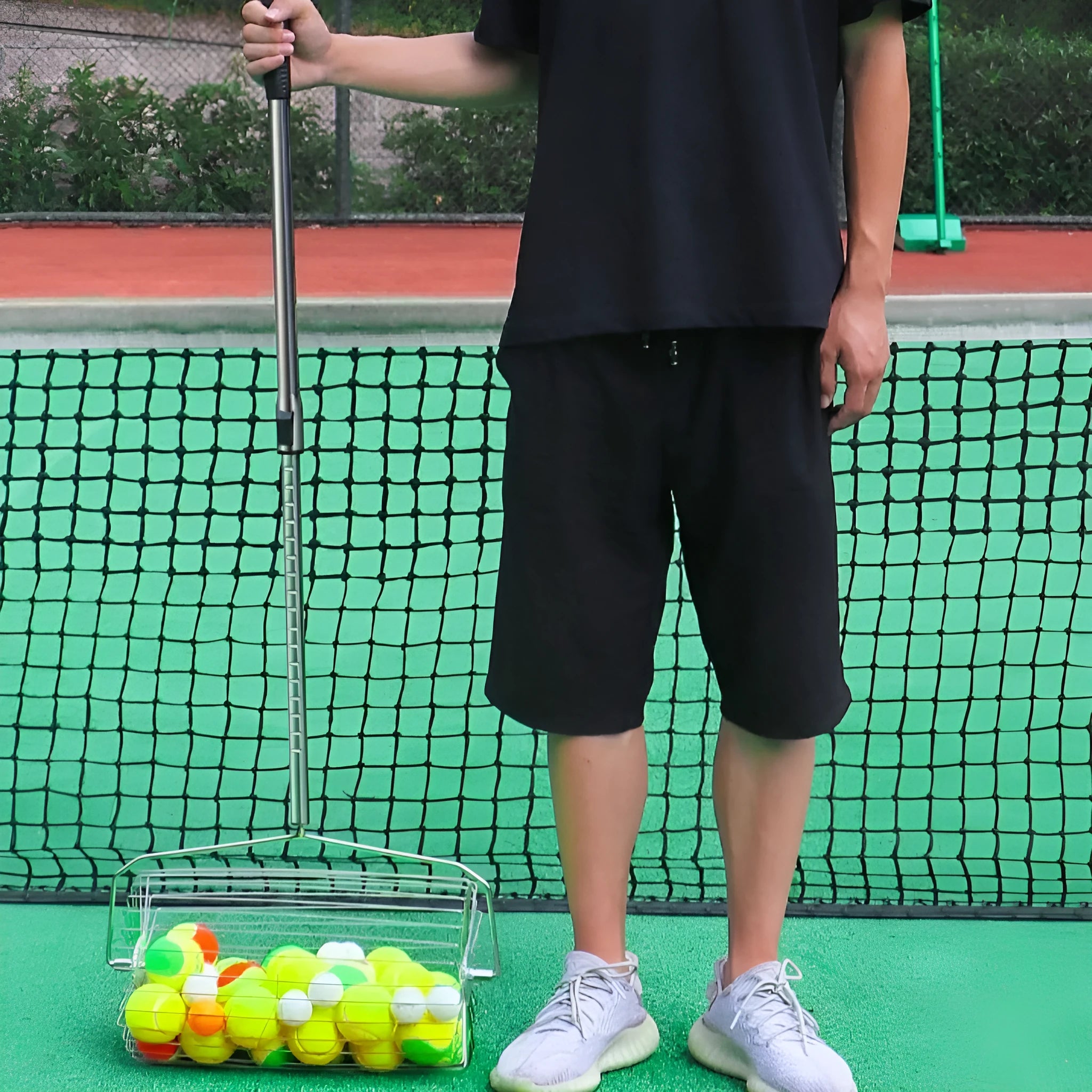 Stainless steel tennis ball picker with adjustable rod holding multiple yellow tennis balls on a court