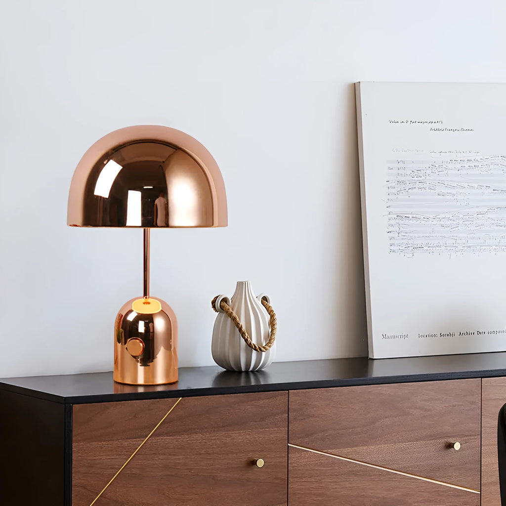 Mushroom-shaped metal table lamp in a rose gold finish on a wooden surface.
