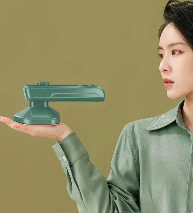 Dark green portable handheld steam iron with ceramic panel, shown next to clothing on a hanger.