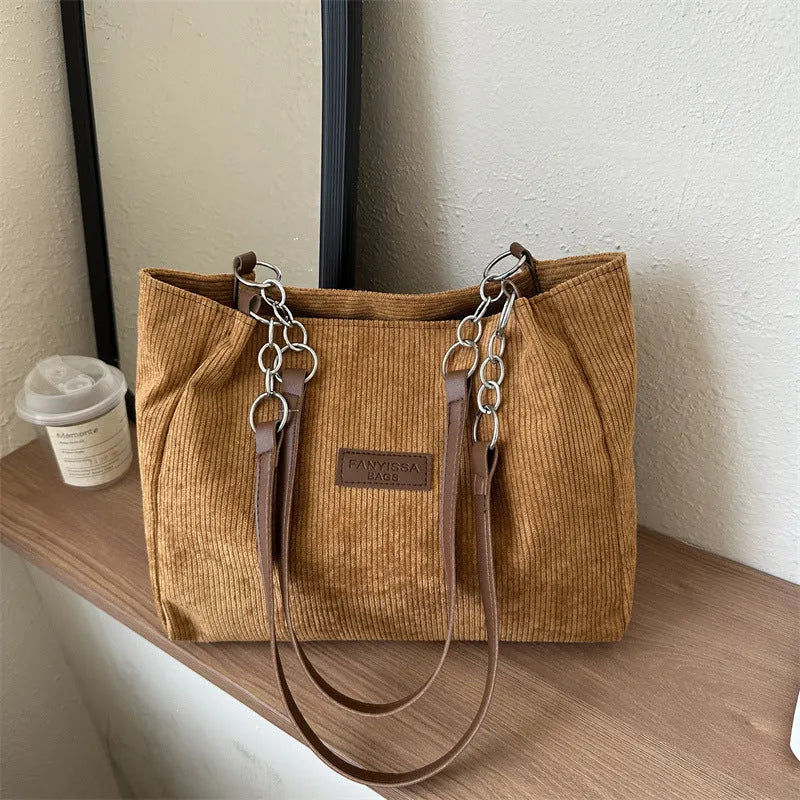Corduroy one-shoulder tote handbag in black, showing three-dimensional pockets and a large main compartment.
